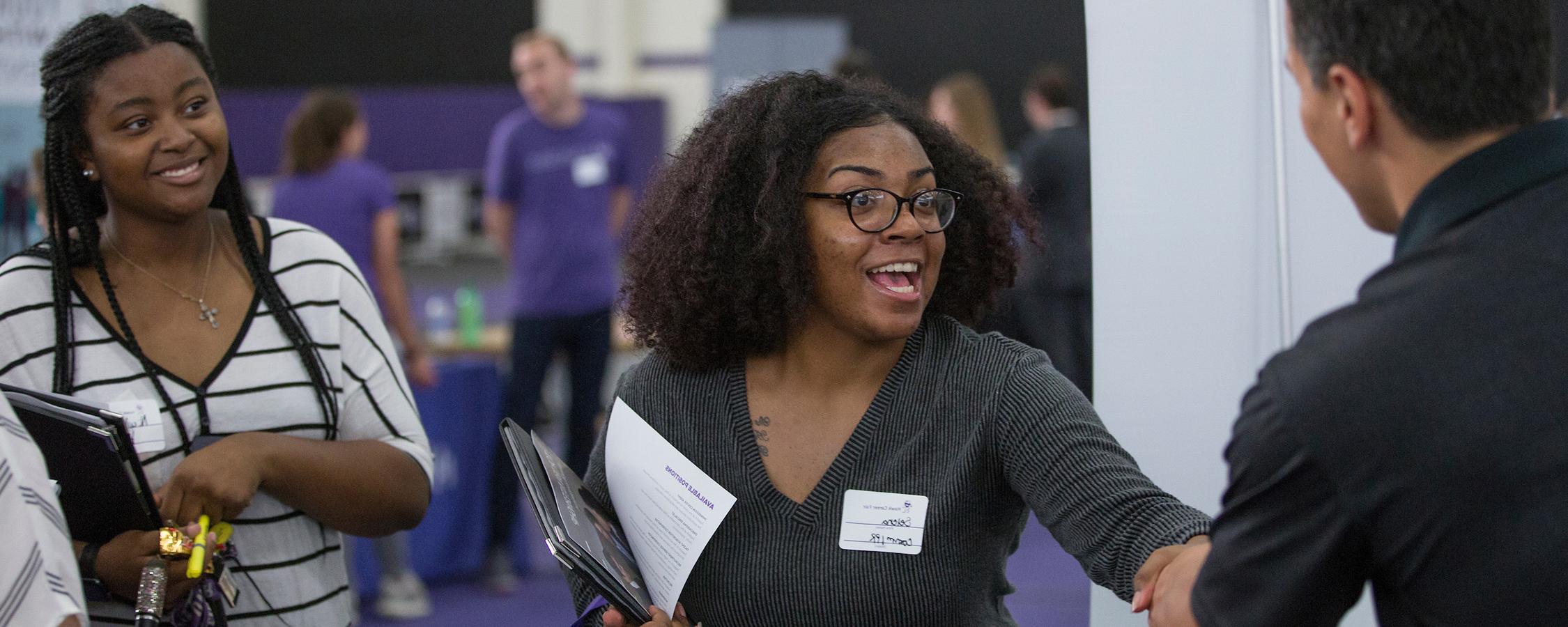 Two women at a career fair shaking hands with a man just out of the frame