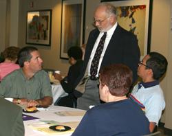 A man standing, talking to a group sitting at a table.